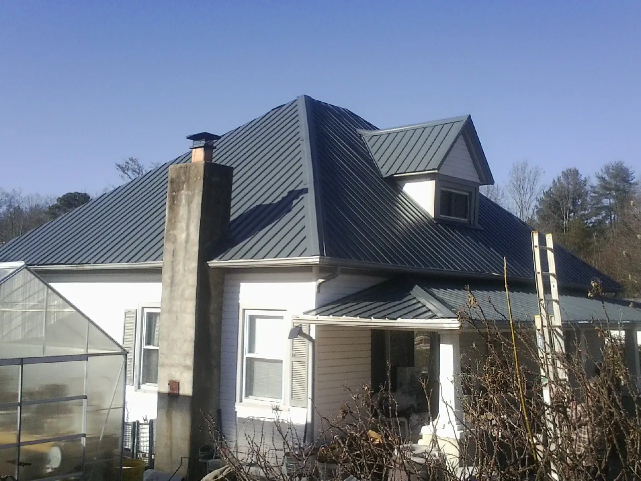 Dark blue standing seam metal roof on a white farmhouse with dormer — Slate & Tile Roof Repair by Roofing Brothers in Delano