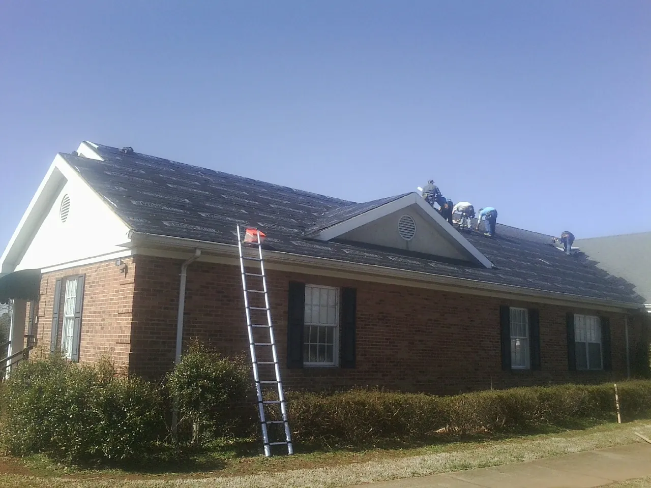 Crew tearing shingles off a brick ranch roof with a ladder set — Emergency Roof Repair work by our crew in Delano