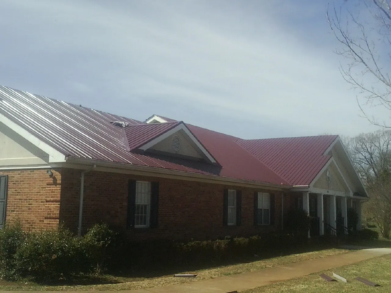Red metal roof with gabled entries on a long brick building, from a Hail Damage Roof Repair job in Delano