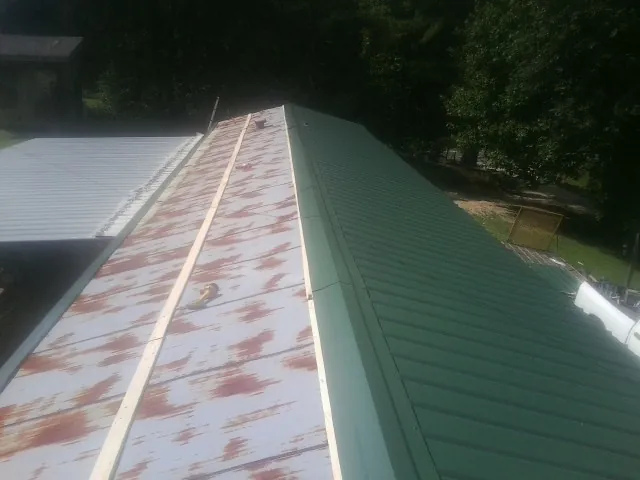 Old rusted panels beside newly installed green metal roofing — Wind Damage Roof Repair by Roofing Brothers in Delano