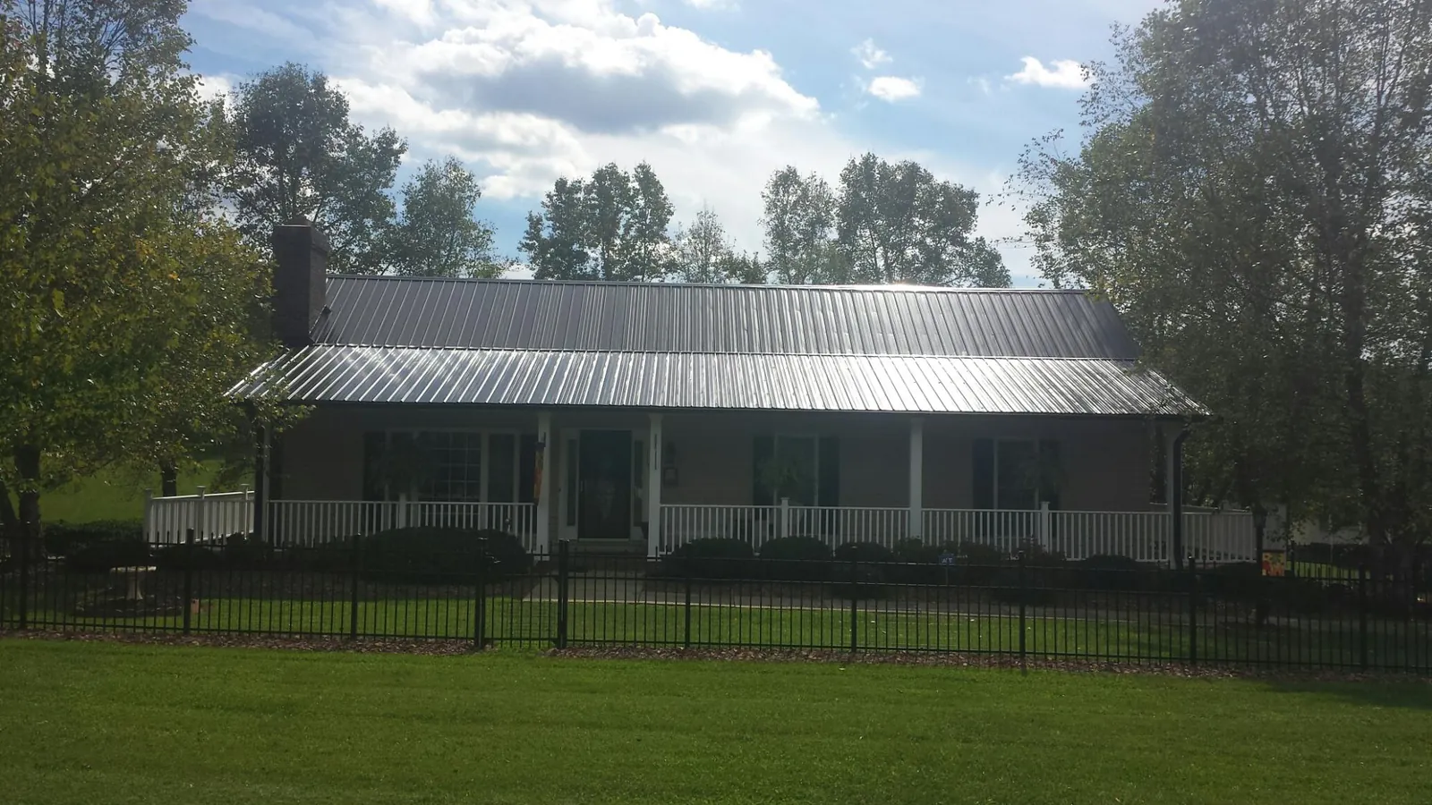 Gray metal roof on a brick ranch with a full width front porch — Gutter Guard Installation work by our crew in Delano