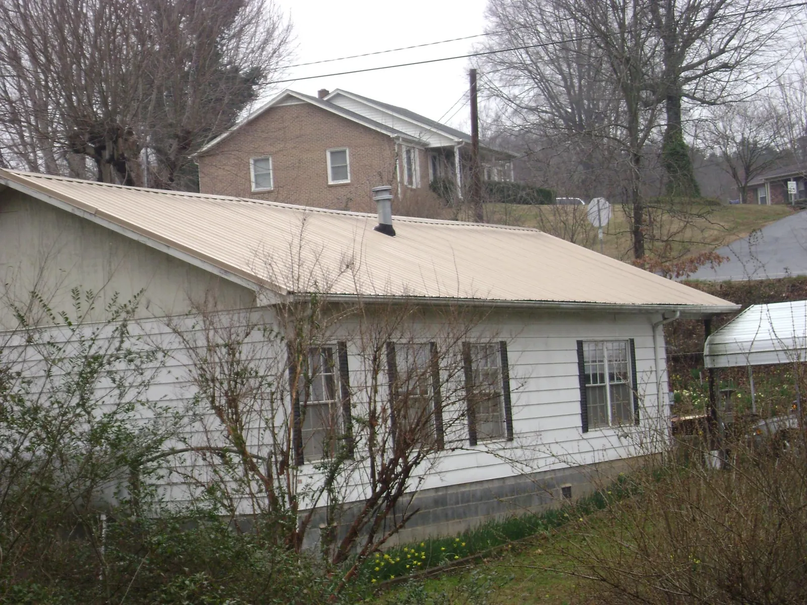 Tan metal roof on a white sided house set into a hillside — Commercial Roofing by Roofing Brothers in Delano